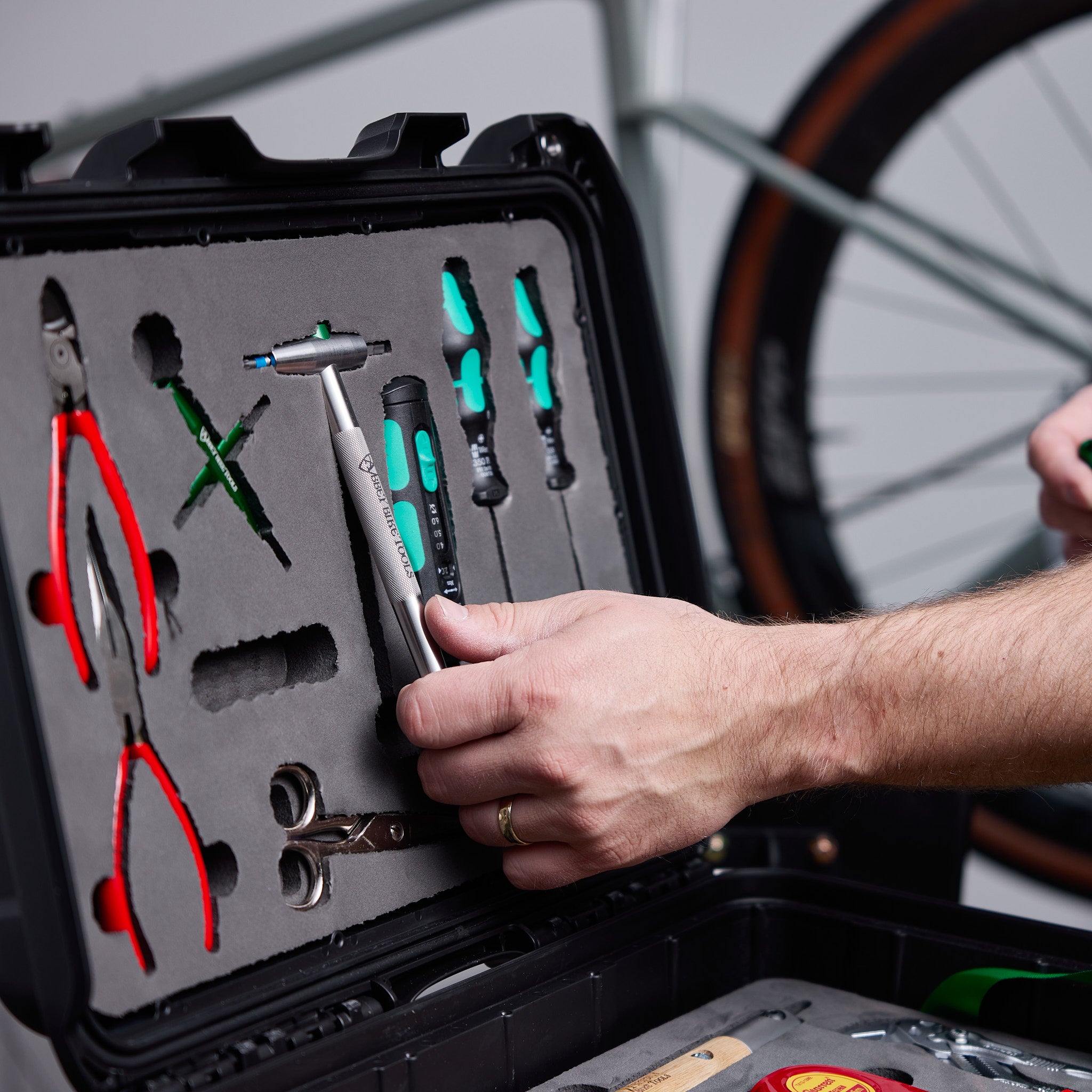Person selecting a tool from an open toolbox with a bicycle in the background